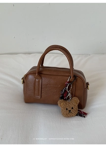 Dettaglio di una borsa boston in pelle marrone con ciondolo a forma di orso e scritte