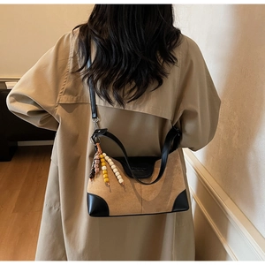 Detail of suede crossbody bag with ethnic bead charm and contrasting black leather trim