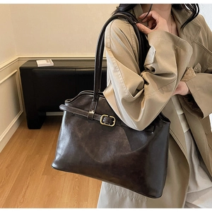 Détail d'un sac cabas marron foncé avec boucle dorée sur un mannequin en trench-coat