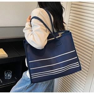 Large striped canvas tote bag in navy blue and white shown on a model in a minimal room