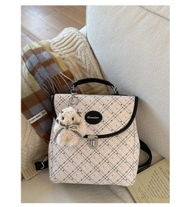 Detail of checkered leather backpack featuring a metal buckle and cute pink plush bunny charm
