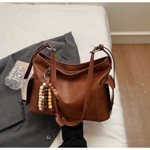 Detail of retro brown hobo bag featuring natural leather texture and ethnic beaded charm