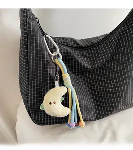 Détail d'un pendentif lune en peluche avec glands colorés sur un sac à carreaux
