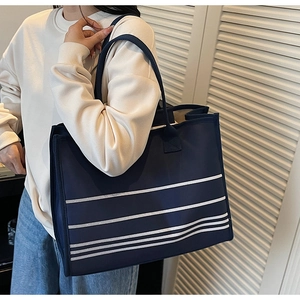 Detail of navy blue striped canvas tote bag worn by a model in a minimalist setting