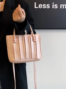Pink pleated bucket bag with round decorative buckles shown on a black suit model