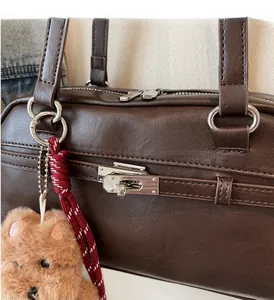 Close-up of brown leather Boston bag featuring silver hardware and a cute plush bear charm