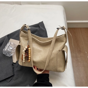 Detail view of beige PU leather bucket bag featuring vintage wooden bead charm and side pockets
