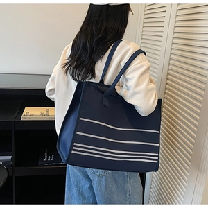 Detail of a large striped navy blue canvas tote bag worn by a model in a lifestyle setting