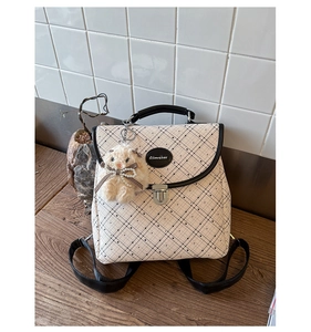 Detail shot of plaid backpack with black trim and cute beige plush rabbit keychain accessory