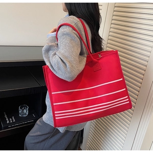 Model showing large red striped canvas tote bag with white stripes and shoulder straps