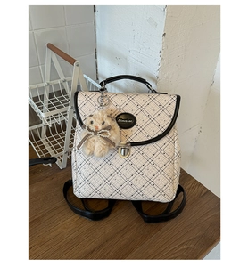 Detail view of plaid backpack with black piping, metal lock, and cute bunny charm