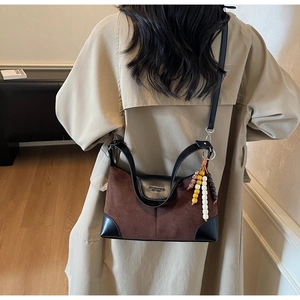 Detail of a brown suede crossbody bag with colorful bead charm and leather shoulder strap