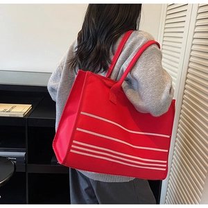 Detailed view of large red canvas tote bag with white stripes on a casual shoulder model