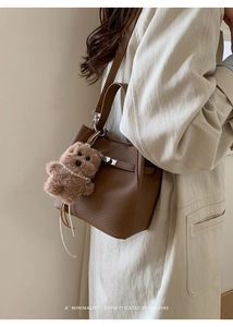 Detail of brown lychee leather bucket bag with a cute plush dog charm on the strap