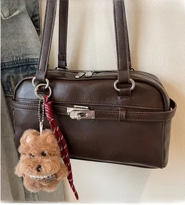 Detailed view of brown leather bag with silver buckle and plush bear pendant detail