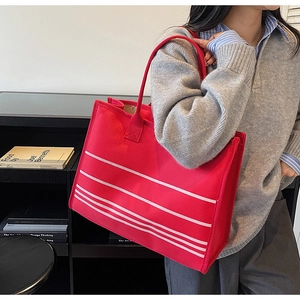 Red canvas tote bag with white stripes shown worn by model in a minimalist setting