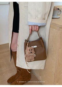 Detail of a brown lychee leather bucket bag with silver twist lock and plush bear charm