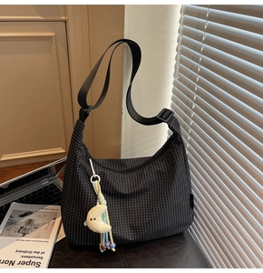 Détail du sac croissant noir à carreaux avec pendentif lune et pompon sur un bureau