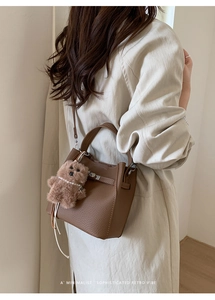 Brown lychee grain leather bucket bag with plush bear charm worn by a model in a trench coat