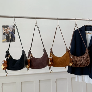 Hobo bags in suede texture with bear charms hanging on a rack in minimalist setting