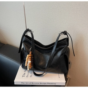 Close-up of black matte leather tote bag side pocket with wooden bead tassel detail