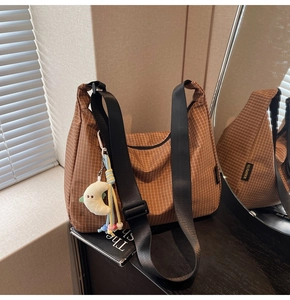 Détail d'un sac hobo en toile à carreaux marron avec pendentif lune sur bois foncé