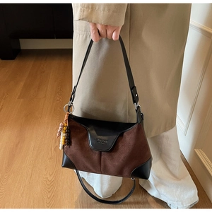 Detail of retro color-block handbag with brown suede texture and ethnic beaded charm