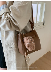 Detail of brown lychee leather bucket bag with a cute plush bear charm and pearl detail
