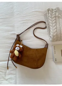 Detailed top view of a brown suede crescent bag with a plush bear charm on white linen