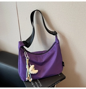 Gros plan du sac violet à carreaux avec pendentif lune sur un livre noir