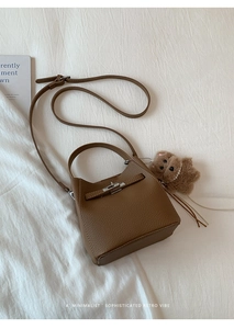 Detail of brown lychee leather bucket bag with metal turn-lock and teddy bear charm