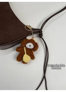Detail view of the brown suede half-moon bag with a cute detachable teddy bear charm