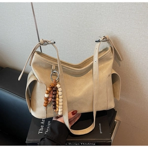 Close-up of minimalist cream dumpling bag with textured pleats and ethnic tassel detail