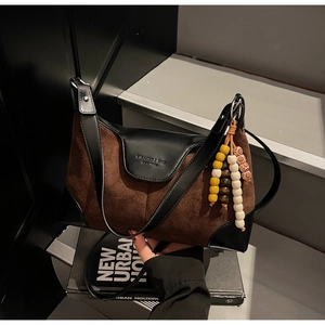 Detail of brown suede and black leather handbag featuring bead tassel and logo embossed flap