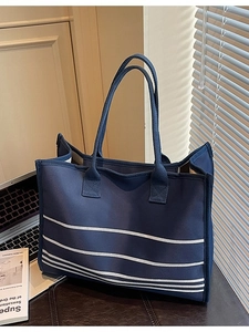 Large navy canvas tote bag with white stripes next to a laptop in a cozy office setting
