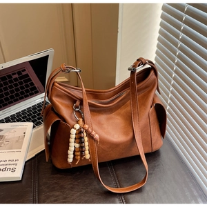 Detail of brown vintage large tote bag side pocket with wood bead charm on a desk