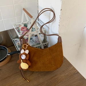 Detail of a brown suede crescent bag with leather trim and a cute plush bear pendant