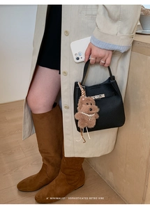 Detail view of black lychee leather bucket bag with silver lock and plush puppy charm