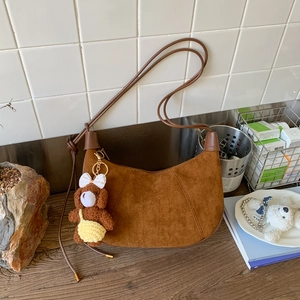 Detail of a brown suede crescent bag with a cute teddy bear charm in a lifestyle setting