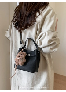 Close-up of black lychee grain leather bucket bag with silver lock and bear charm
