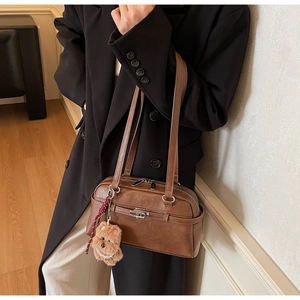 Detail shot of brown leather Boston bag with plush bear charm worn with black coat