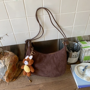 Close-up of dark brown suede half-moon bag with cute brown bear charm and white bow