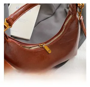 Détail du fermoir doré et de la texture cuir sur ce sac demi-lune marron élégant