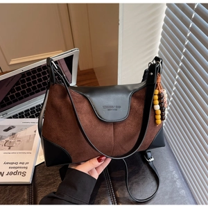 Detail of a brown suede handbag with black leather accents and a beaded retro charm