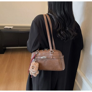 Detail view of a vintage brown shoulder bag featuring a cute teddy bear charm and metal clasp