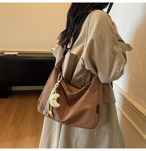 Sac à main en toile à carreaux marron avec pendentif lune blanche porté à l'épaule