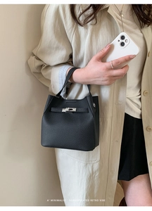 Detail of black lychee grain leather bucket bag with metal buckle on beige trench coat
