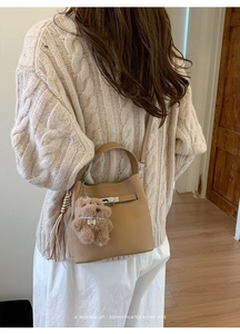 Camel leather bucket bag with metallic twist lock and cute plush bear charm on model