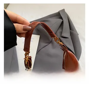 Gros plan du sac hobo en cuir marron avec ferrures dorées et détail de pompon décoratif