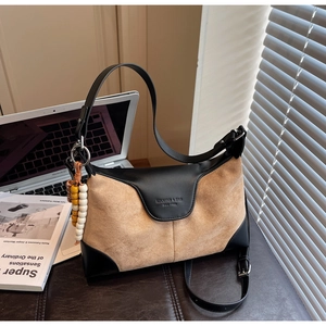 Detail of camel suede handbag with black leather trim and decorative wooden bead charm